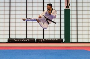 martial artist kicking in the air above a blue mat
